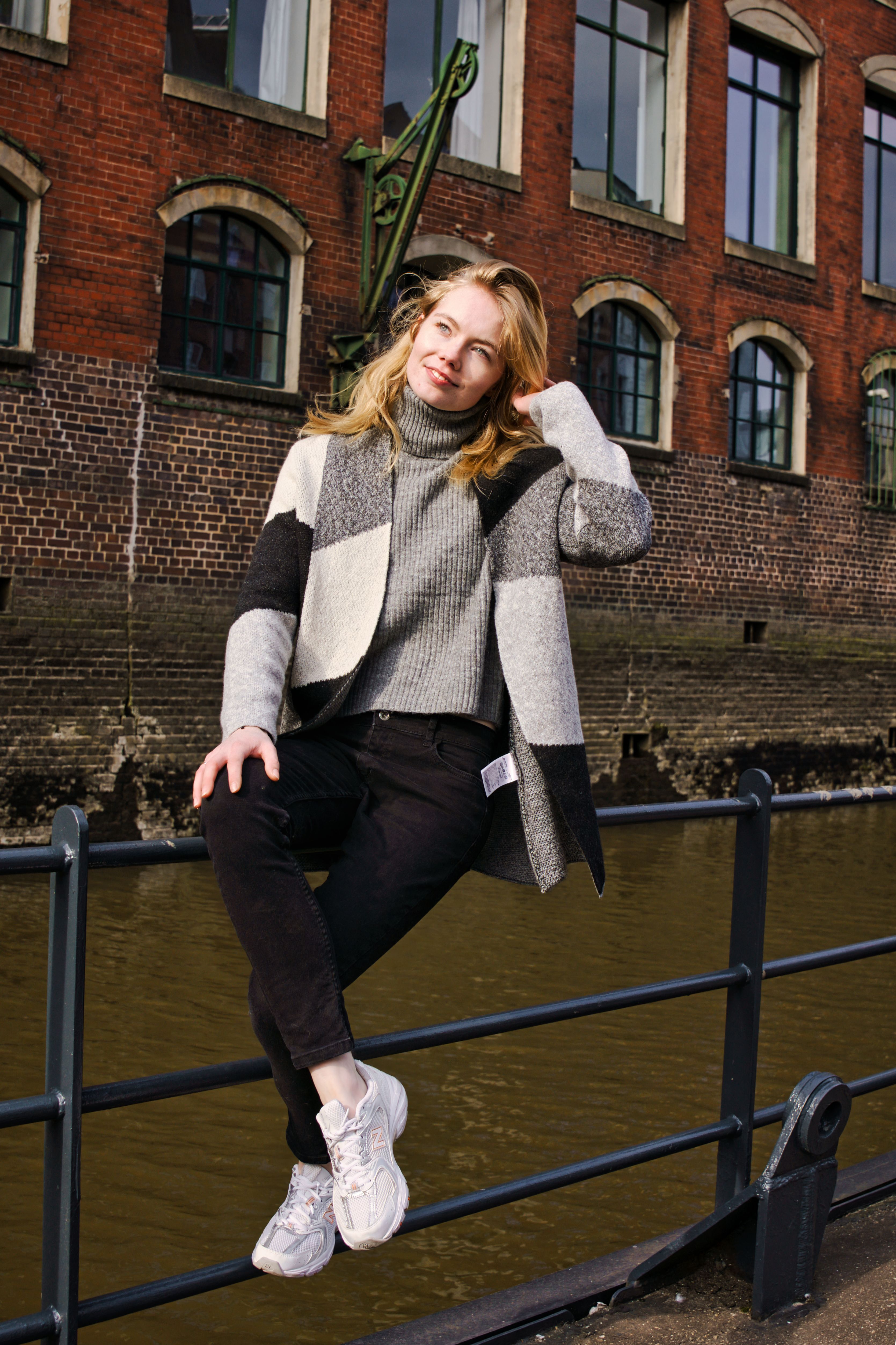 Stylish woman sitting by a canal in Hamburg, Germany, wearing casual attire on a sunny day.