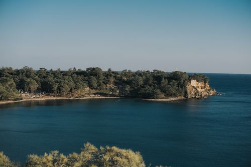 Free A tranquil view of an island surrounded by calm blue waters and lush greenery under a clear sky. Stock Photo