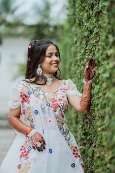 Joyful woman in traditional outfit adorned with henna, touching lush greenery.