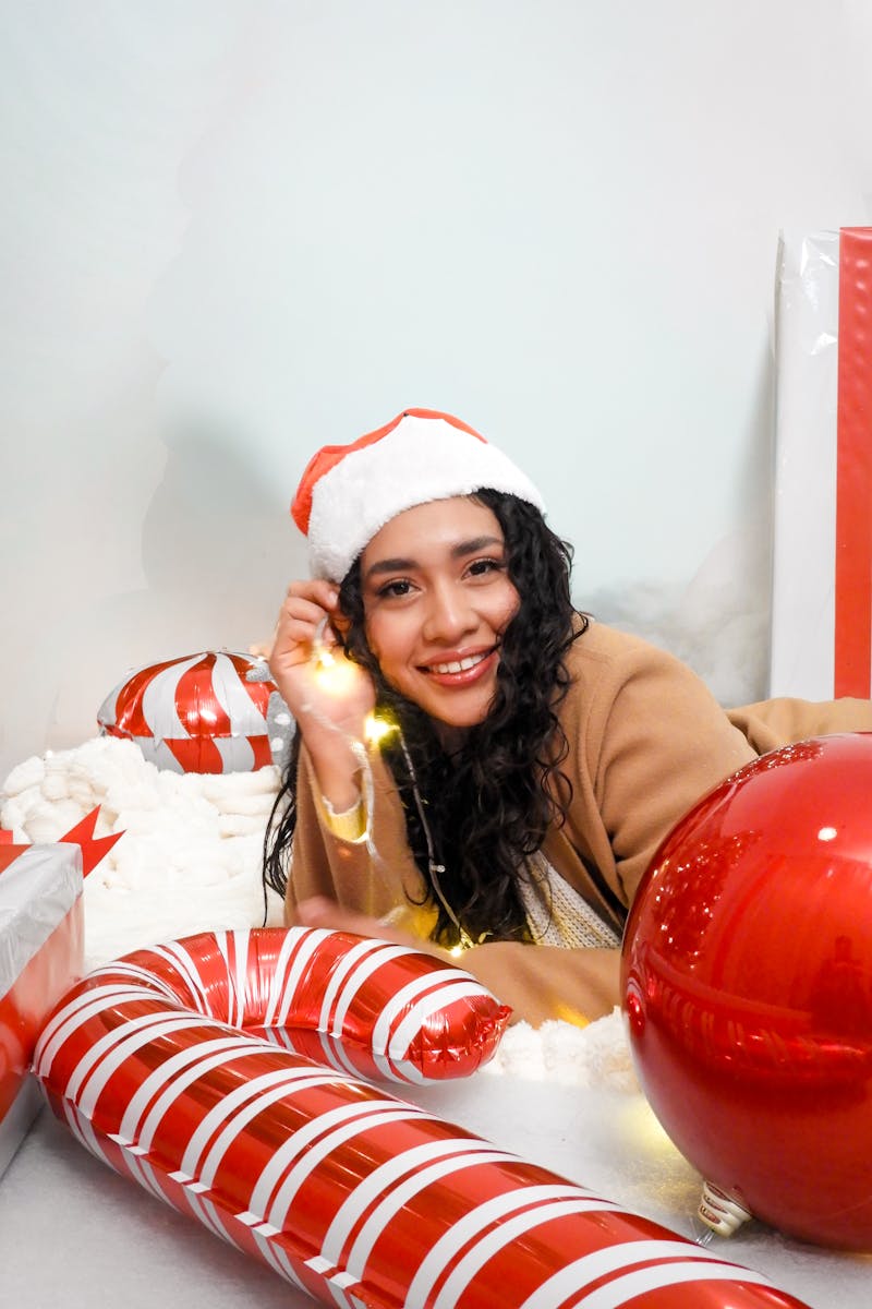 A joyful woman in a Santa hat surrounded by festive Christmas decorations and gifts.