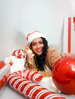 A joyful woman in a Santa hat surrounded by festive Christmas decorations and gifts.