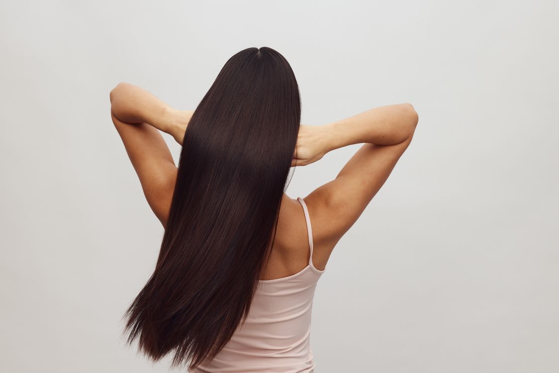 Free Asian woman with long, straight hair shown from behind, embracing hair care and beauty. Stock Photo