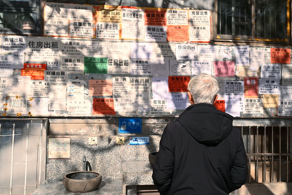 年配の男性が、日光の下で都市生活を浮き彫りにする壁の賃貸広告をじっと見つめている。