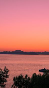 Boat sails on calm sea under a vibrant sunset sky, creating a peaceful seascape.