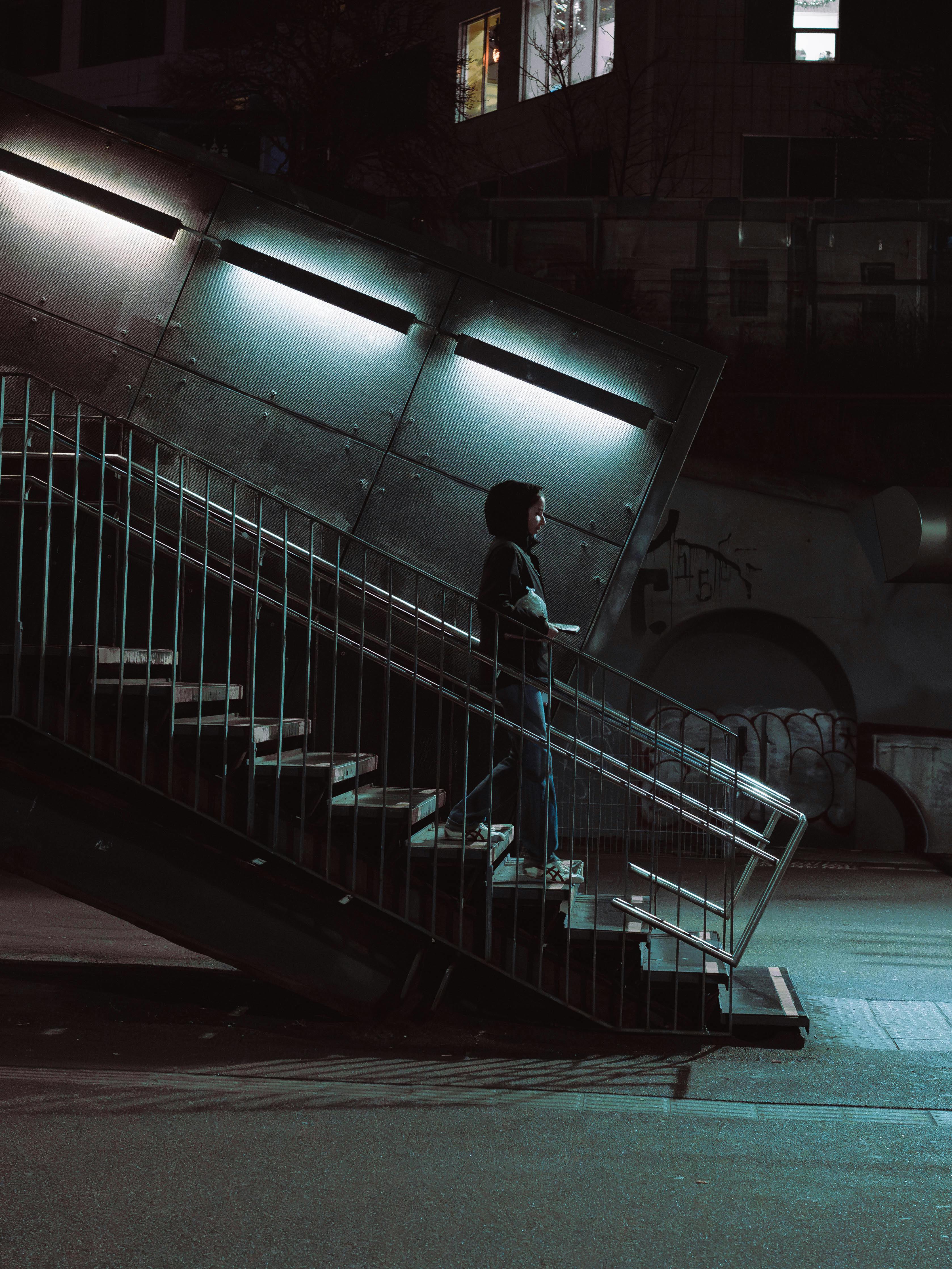 De franc Una persona es troba contemplativament a les escales urbanes a la nit, il·luminades per llums fredes. Foto d'estoc