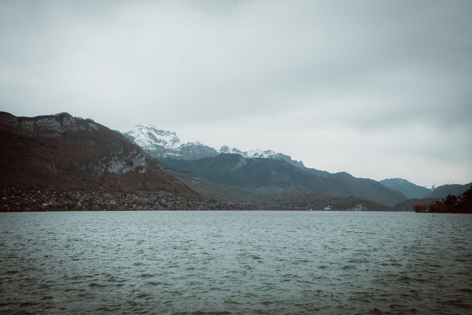Vista tranquila del lago de Annecy con montañas de los Alpes cubiertas de nieve en otoño.