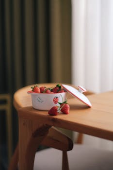 A wooden table indoors featuring a bowl of fresh strawberries, creating a warm, rustic vibe.