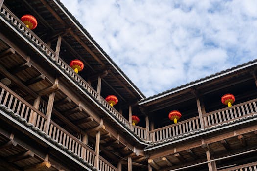 Wooden Tulou building with vibrant red lanterns under a blue sky, showcasing traditional Chinese architecture.