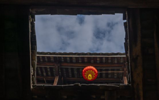 A vibrant red lantern suspended in a traditional courtyard against a cloudy sky.