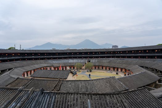 Aerial view of a traditional Chinese Fujian Tulou with mountainous background on a cloudy day.