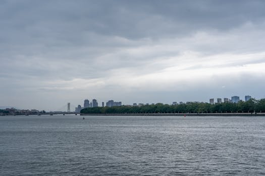 A serene view of a cityscape with a river and cloudy sky, showcasing modern architecture.