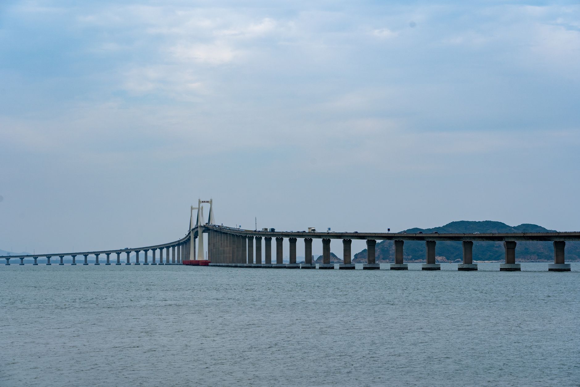 Long stretch of a modern suspension bridge over the sea with a cloudy sky.