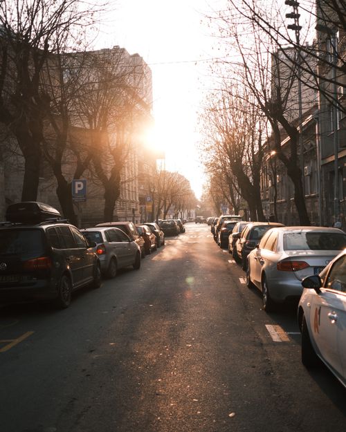 Free A serene urban street scene with cars parked along the sides, bathed in warm sunset light. Stock Photo