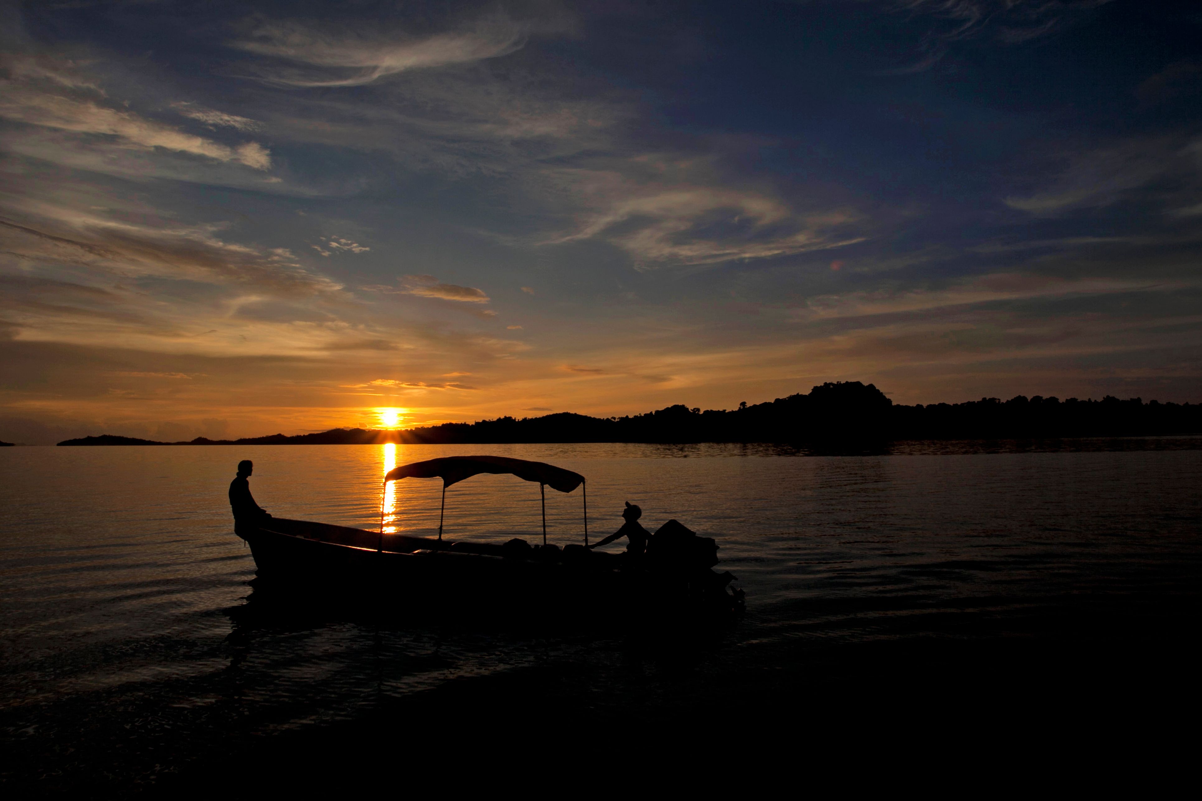 Peaceful sunset view with boat silhouette on a serene lake, perfect for travel and nature themes.