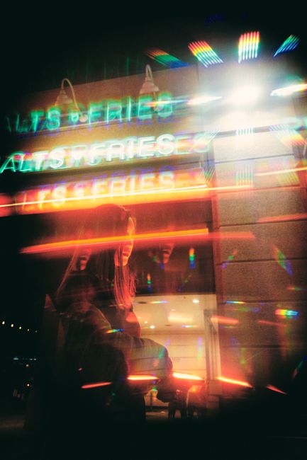 Blurred neon lights reflecting in a city street scene at night, with a person in view.