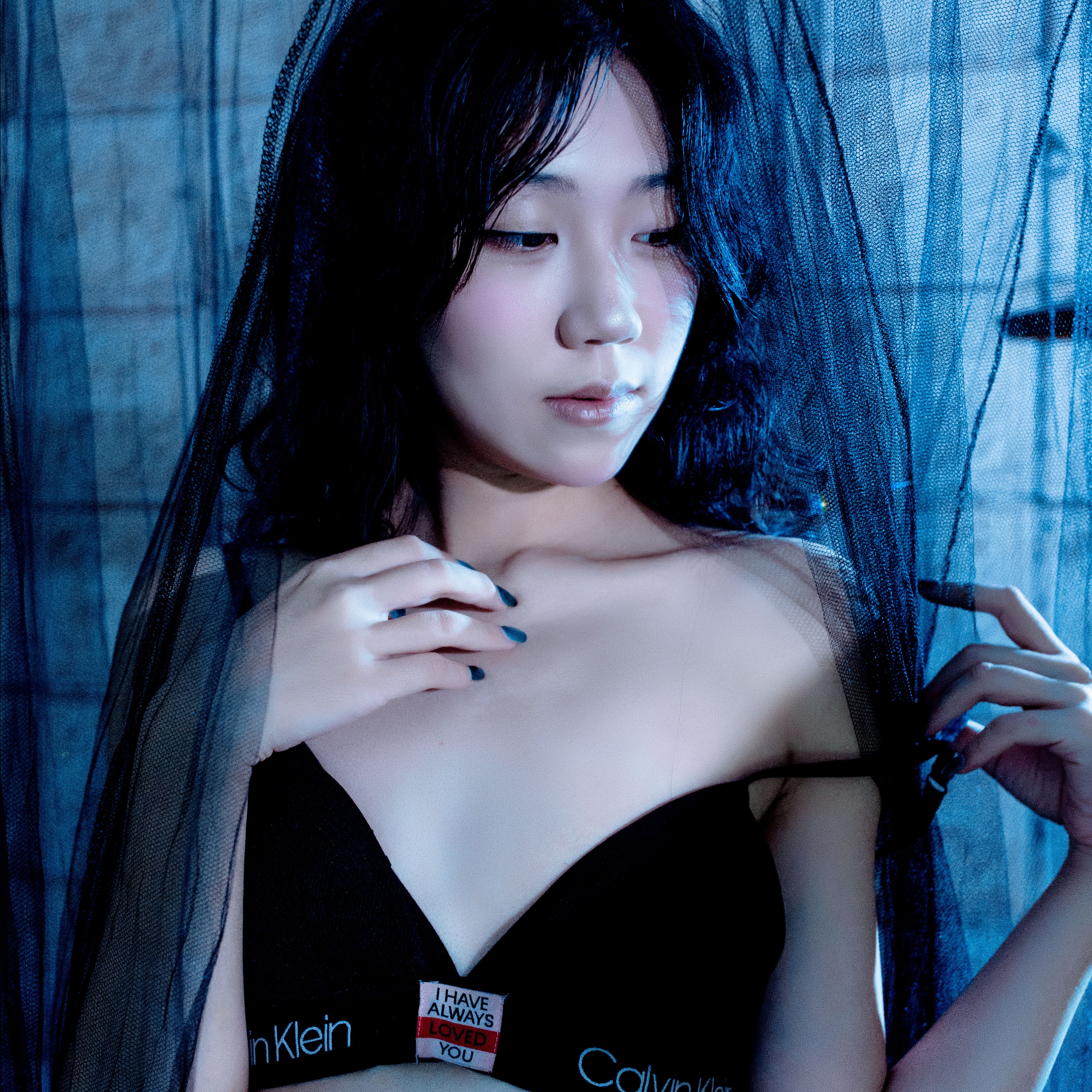 A creative portrait of a woman under a black veil with subdued blue lighting indoors.