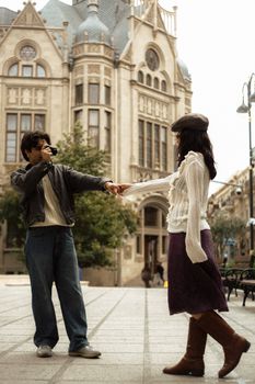 A couple holding hands in front of an ornate historic building, capturing a romantic moment.