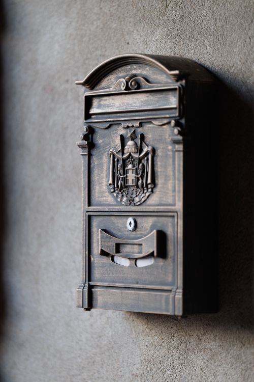 Free Close-up of a vintage bronze mailbox featuring a decorative crest on a textured wall surface. Stock Photo