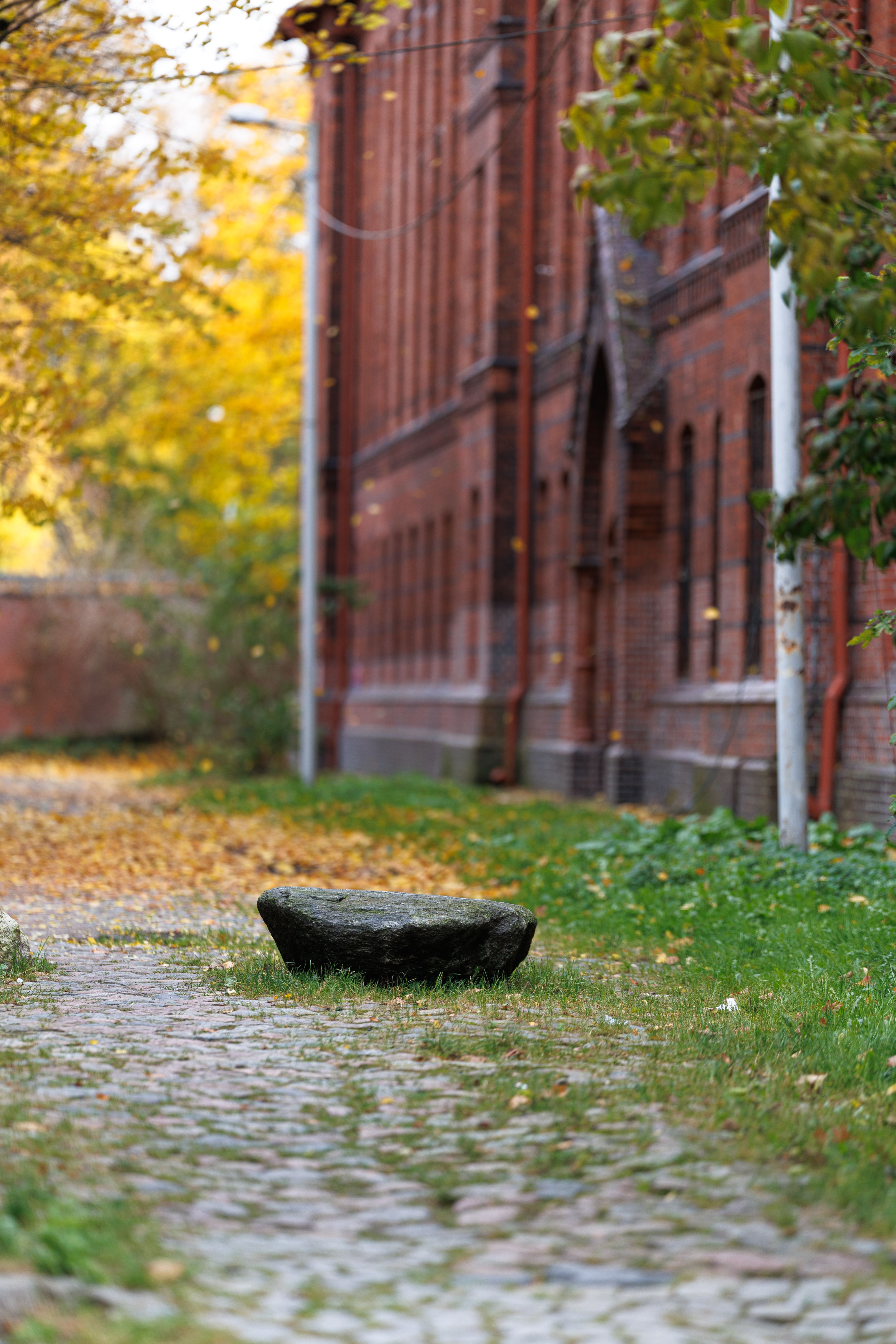 Scenic view of historic red brick building with cobblestone path and autumn foliage.