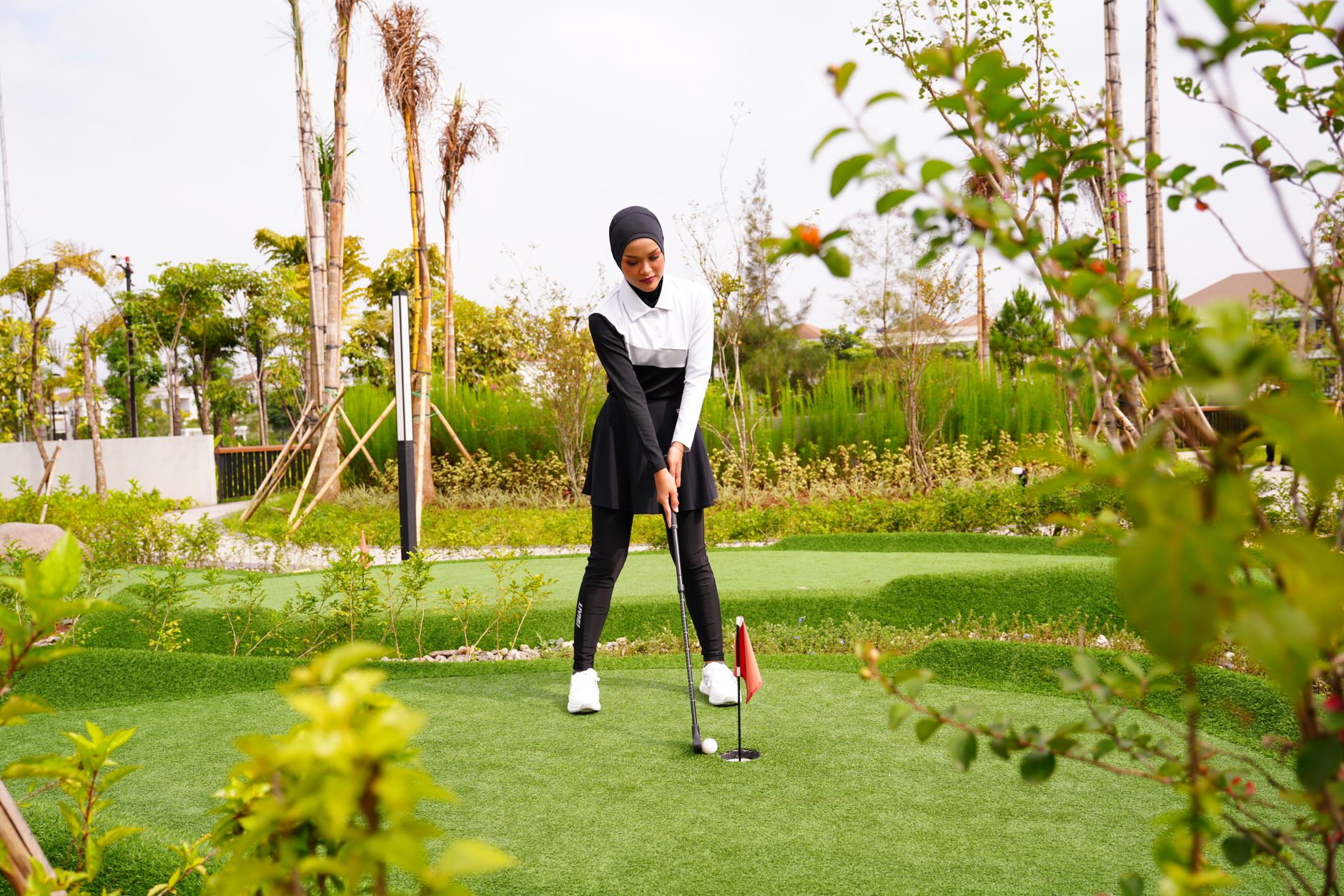 A young Muslim woman in sporty attire playing golf outdoors in Jawa Barat, Indonesia.