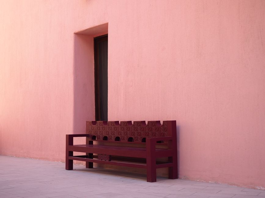 A minimalist outdoor scene with a pink wall and wooden bench in Doha, Qatar.