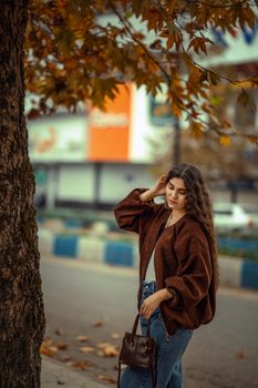 A young woman walking outdoors in autumn, surrounded by a warm, leafy background.