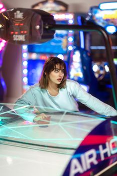 Focused young woman enjoying a game of air hockey in a vibrant arcade setting.