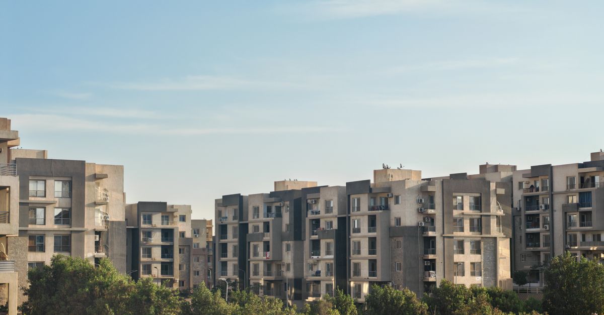 View of modern residential apartment buildings surrounded by trees under a clear blue sky.