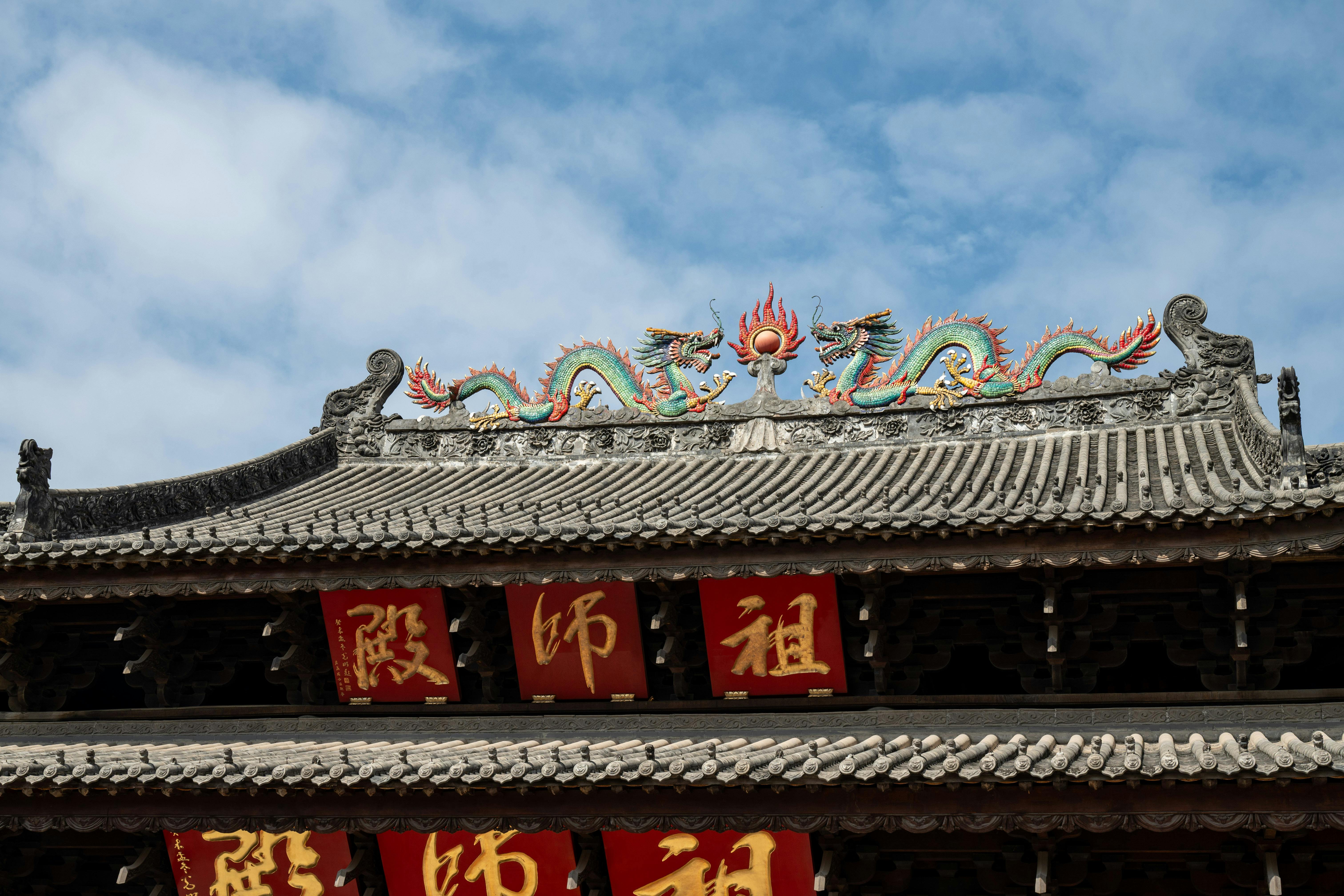 Ornate dragon sculpture atop an ancient Chinese temple roof with red banners, under a clear blue sky. - Guangzhou