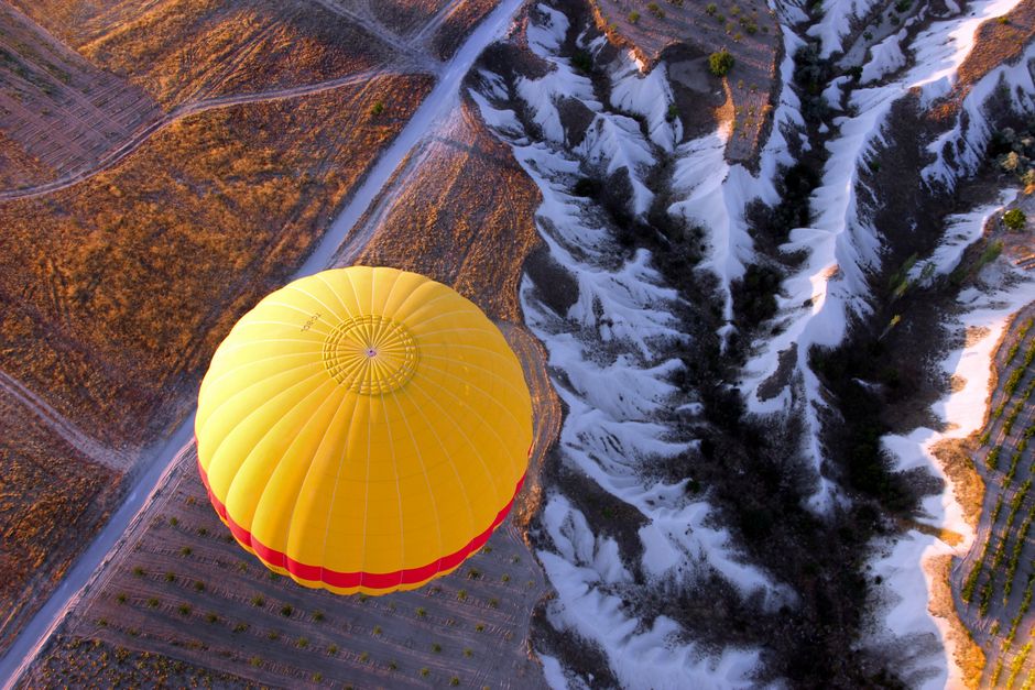 Hot air balloon soaring over the unique rock formations of Cappadocia, Türkiye at sunrise.