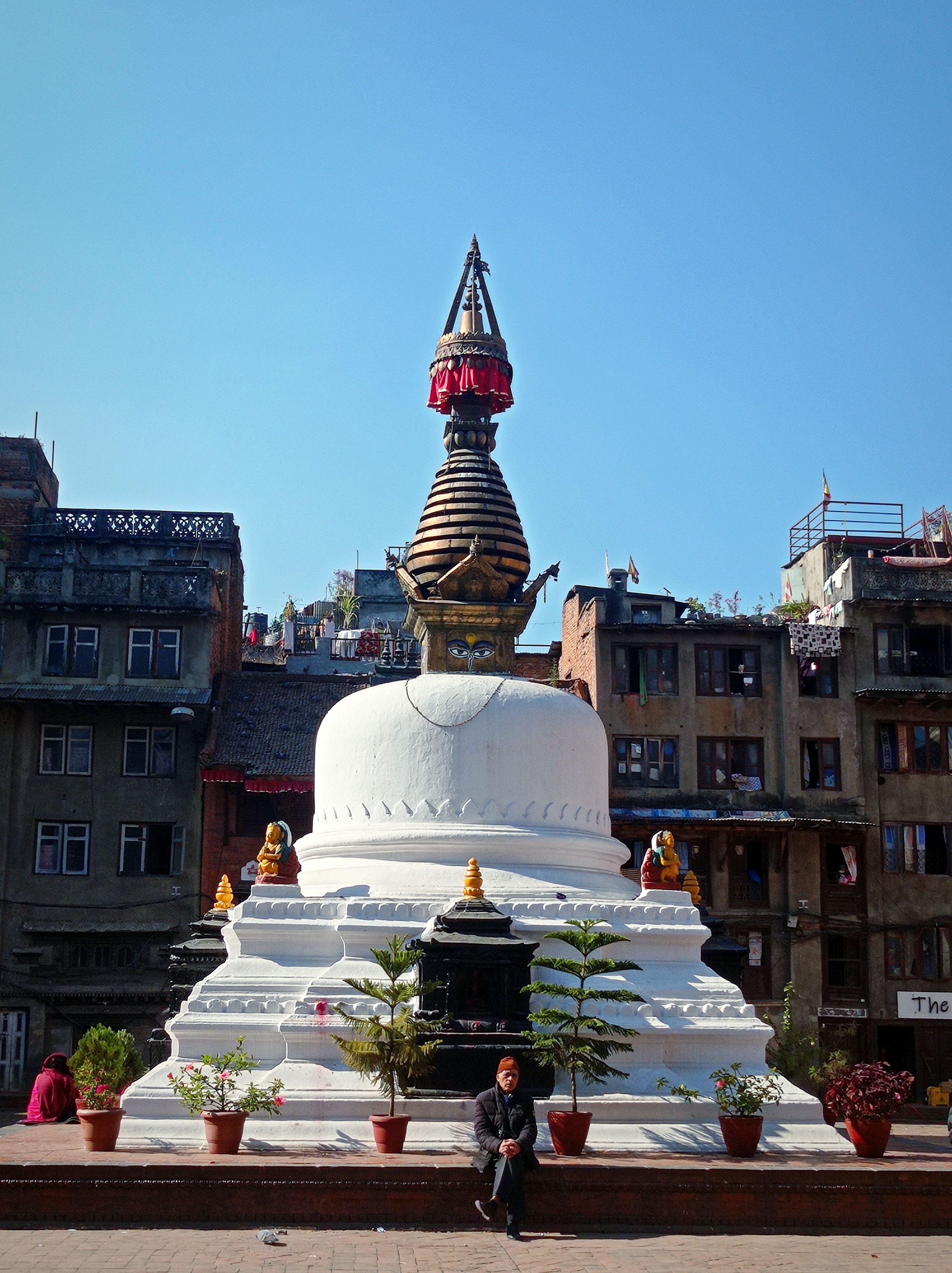 A small whitewashed stupa with a tiered spire in a square of old brick houses in the Kathmandu valley