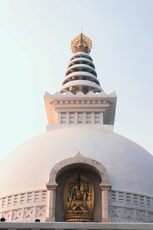 Free A tranquil Buddhist stupa with a golden statue, captured under a clear sky, showcasing spiritual architecture. Stock Photo