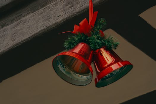Captivating shot of shiny red Christmas bells adorned with festive greenery and ribbon, perfect for holiday decor.