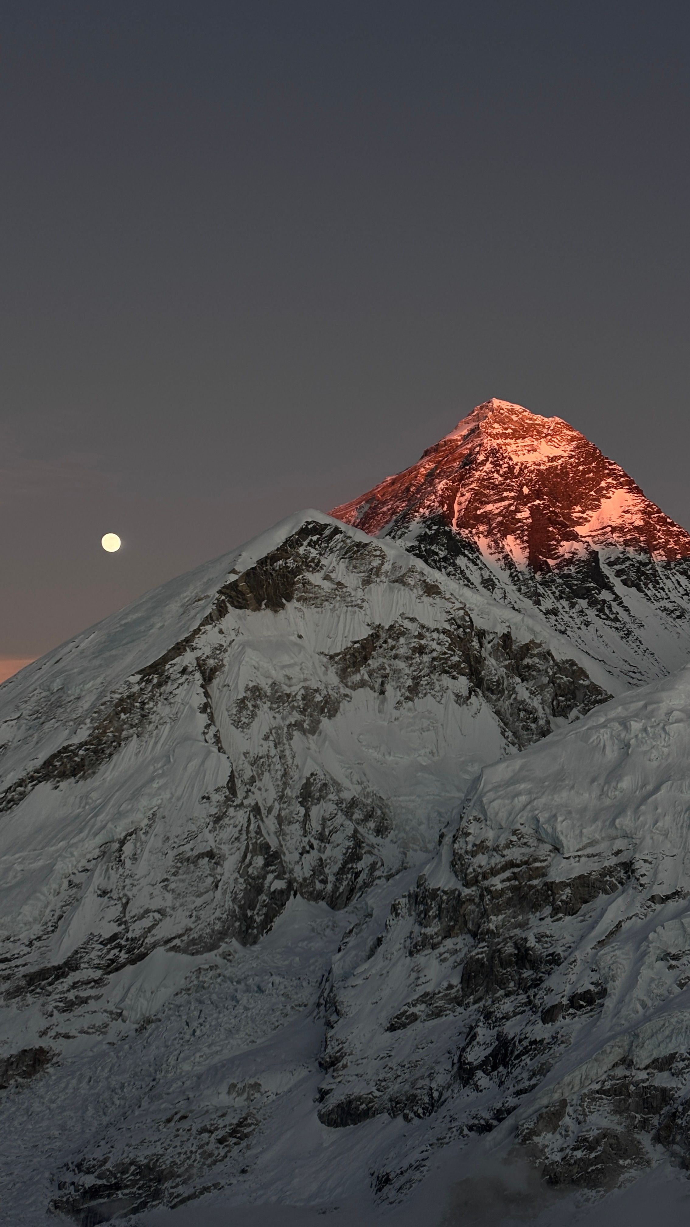 Majestic view of snow-capped Mount Everest at sunset with a full moon in the sky.