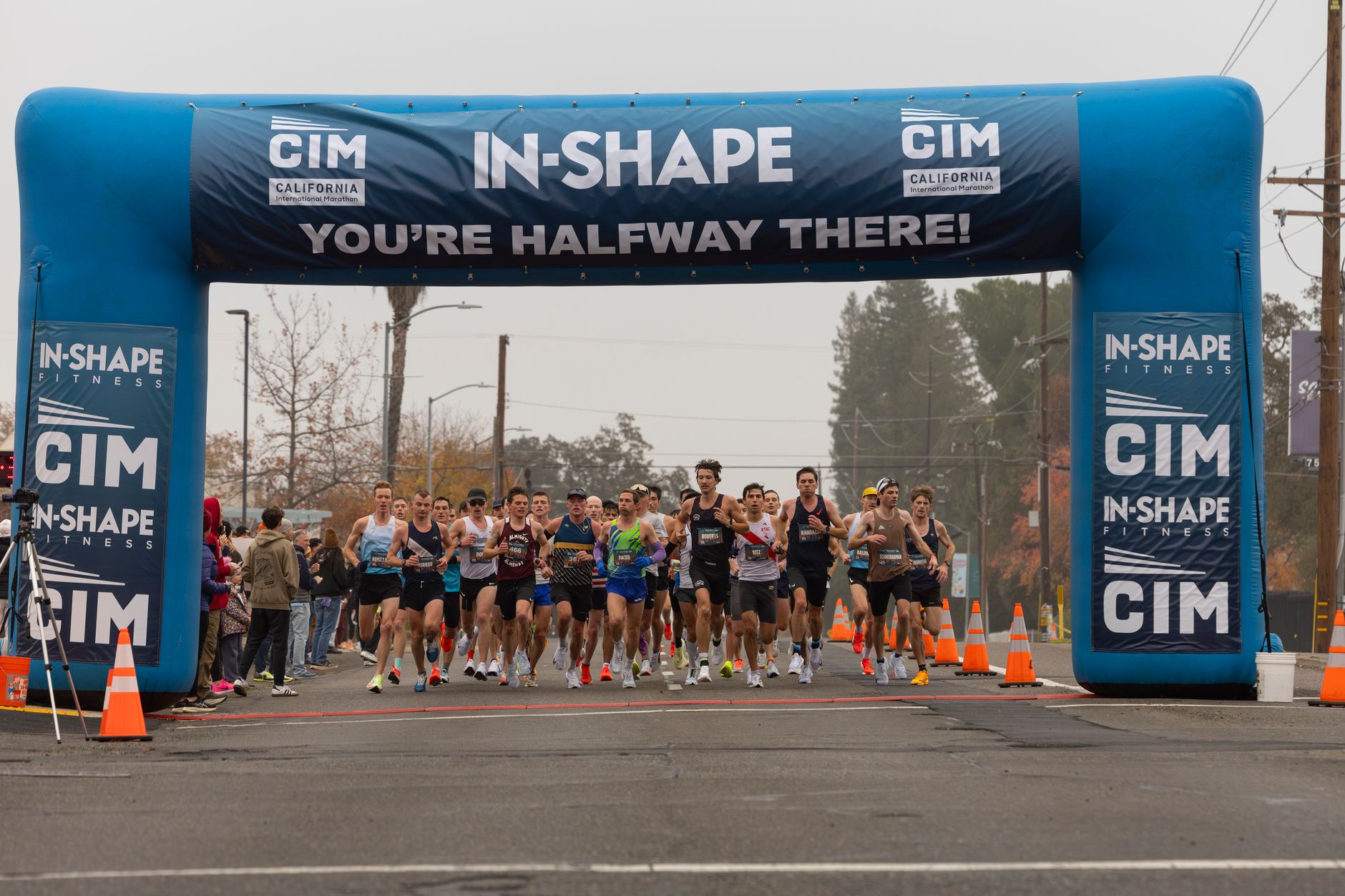 A group of runners reach the halfway mark in a marathon under an inflatable arch.