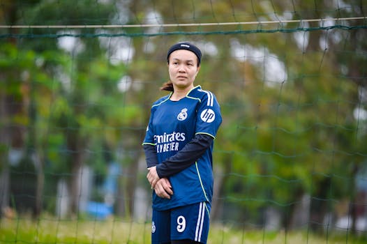 Female soccer player in blue jersey standing on field in Hanoi for a local game.