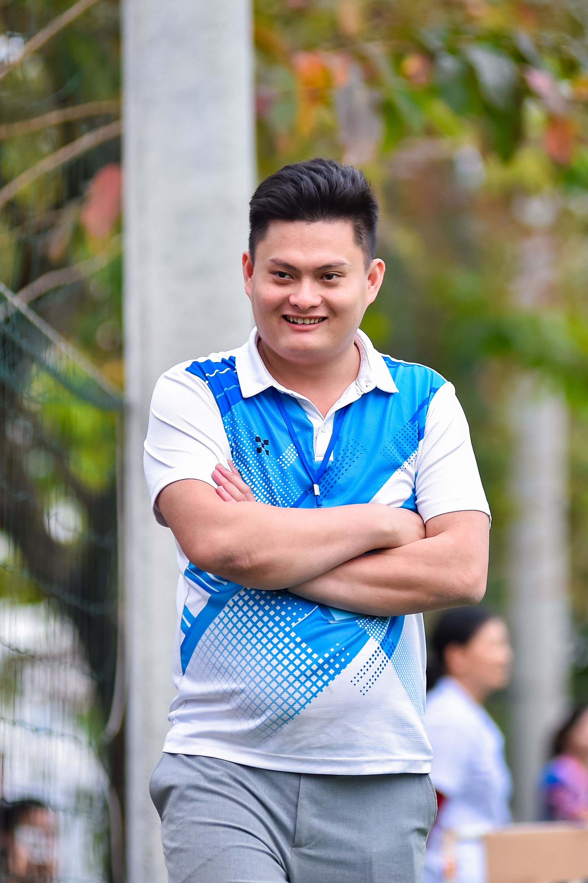 A cheerful man in a blue shirt smiles at an outdoor event in Hanoi, Vietnam.