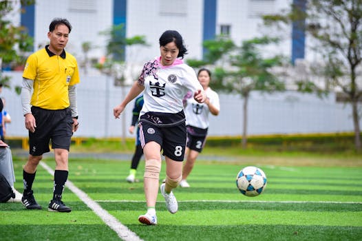 Women soccer players and a referee on a vibrant green field in Hanoi, Vietnam.