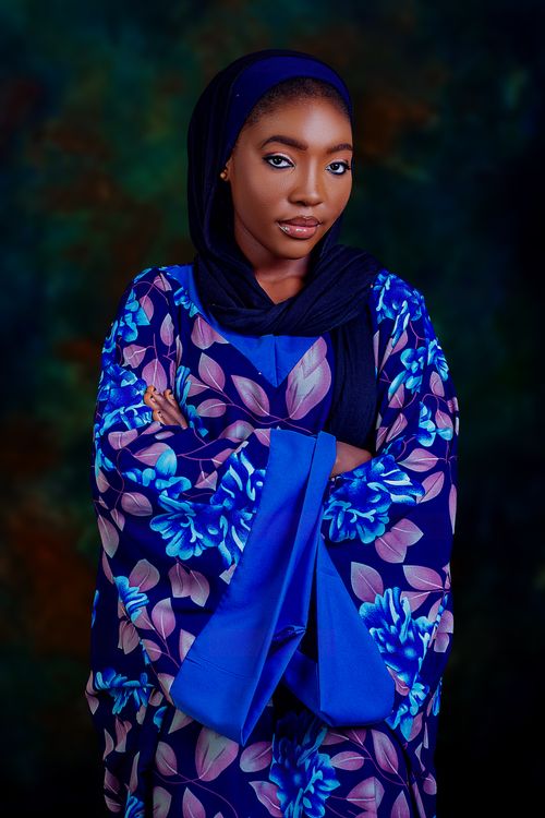 Free Elegant woman in blue and floral dress with dark background, arms crossed. Stock Photo
