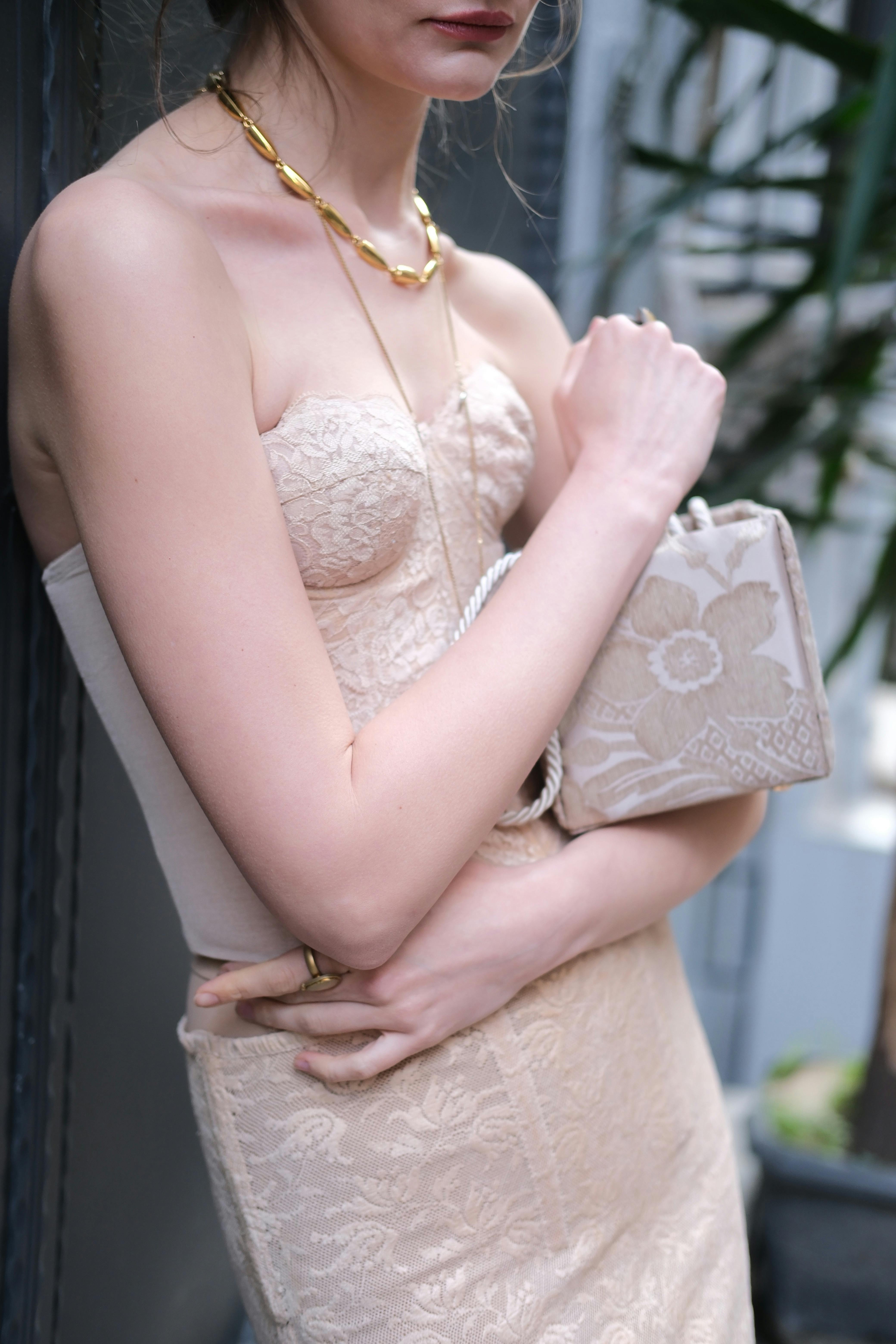 Gratis Elegant og sofistikert kvinne iført blondekjole og holder en beige clutch med blomstermotiv. Arkivbilde