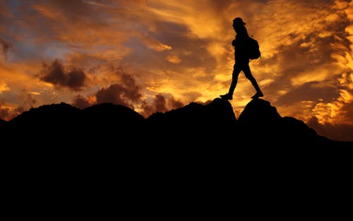 Silhouette of Person Standing on Rock Formation during Sunset