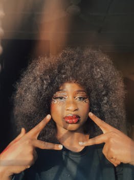 Creative portrait featuring a woman with bold makeup and afro hairstyle in warm lighting.