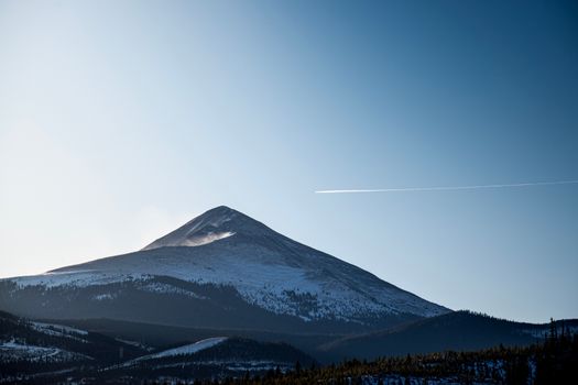 Stunning view of a snow-capped mountain peak under a clear blue sky with a distant contrail.