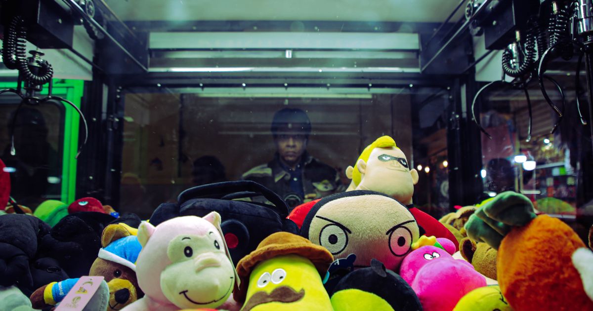 Vibrant plush toys inside a claw machine with a person reflected in the glass.