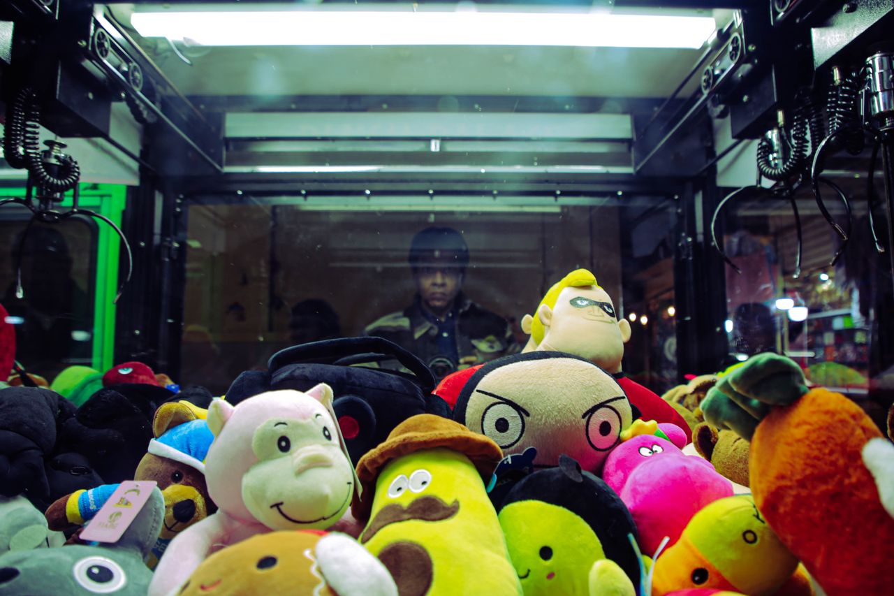 vibrant plush toys inside a claw machine with a person reflected in th
