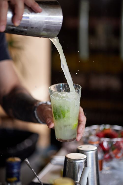 Free Bartender expertly pouring a refreshing mojito cocktail with lime and mint. Stock Photo