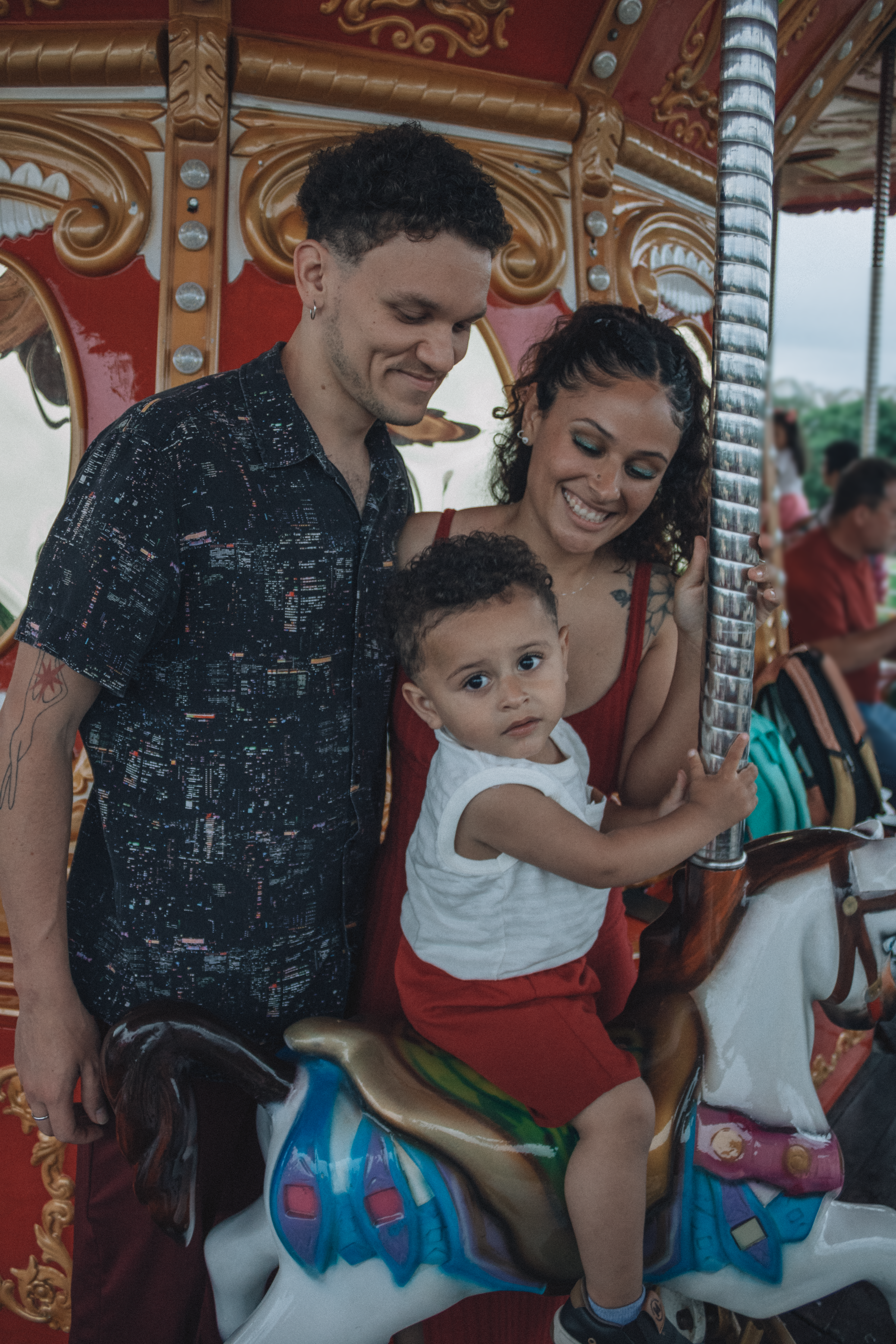 Happy family with child riding a carousel horse in an amusement park setting.