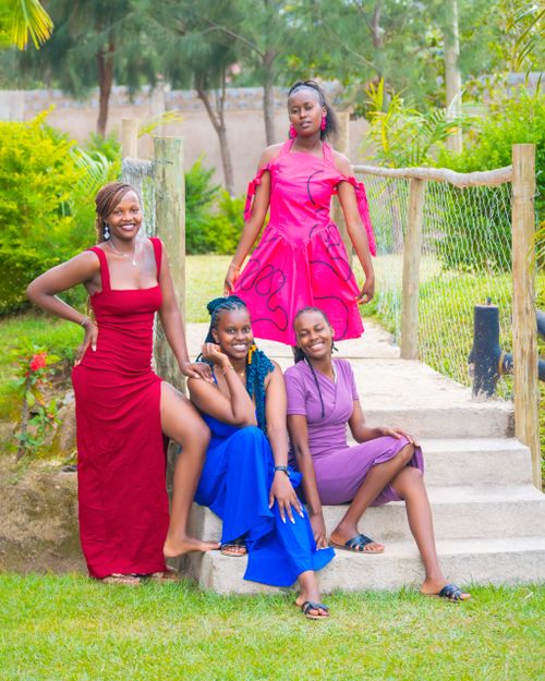 Free Four women posing in vibrant dresses on garden steps, showcasing joy and elegance. Stock Photo