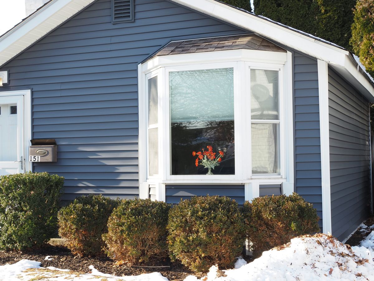 A blue house with a bay window and snow on the ground in winter