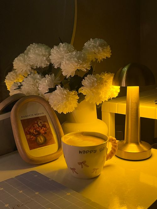 Free Warm evening setting with flowers, lamp, and coffee mug on a desk. Stock Photo